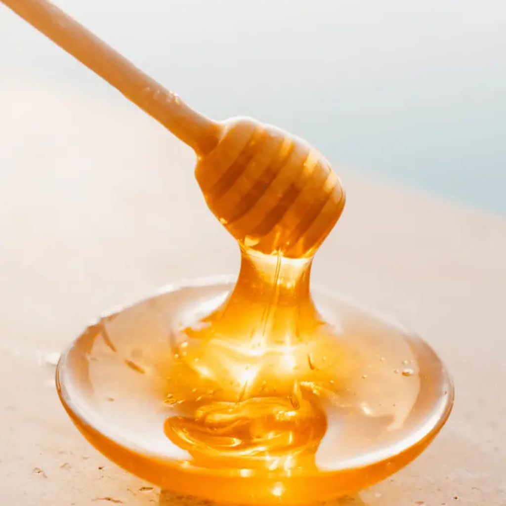 Cremiger Orangenblütenhonig wird mit Honiglöffel aus mit Honig gefülltem Schälchen entnommen